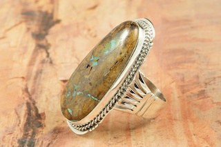 Genuine Boulder Turquoise set in Sterling Silver Ring. The cabachon is Boulder Turquoise, you can see the veins of Turquoise running through the host rock. The Boulder Turquoise Mine is located in northeast Nevada. It was discovered in 1970 by a Shoshone sheep herder. Production is small due to the remote location and winter weather. Boulder Turquoise is valued for both it's beauty and rarity. Every stone is unique. Created by Navajo Artist Lucy Valencia. Signed L. J. by the artist.